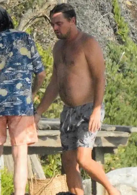 图中的莱昂纳多穿着灰色带有花纹的宽松短裤,露出了他的大肚腩,头发沾