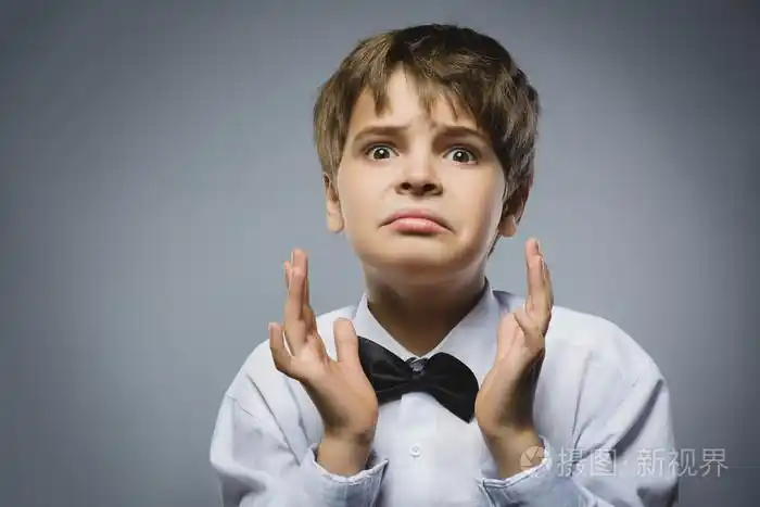 英俊的男孩,而站在灰色背景下的惊讶表情的特写肖像