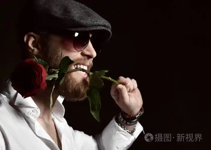 带着胡子戴着帽子的残忍的男人嘴里拿着红玫瑰约会