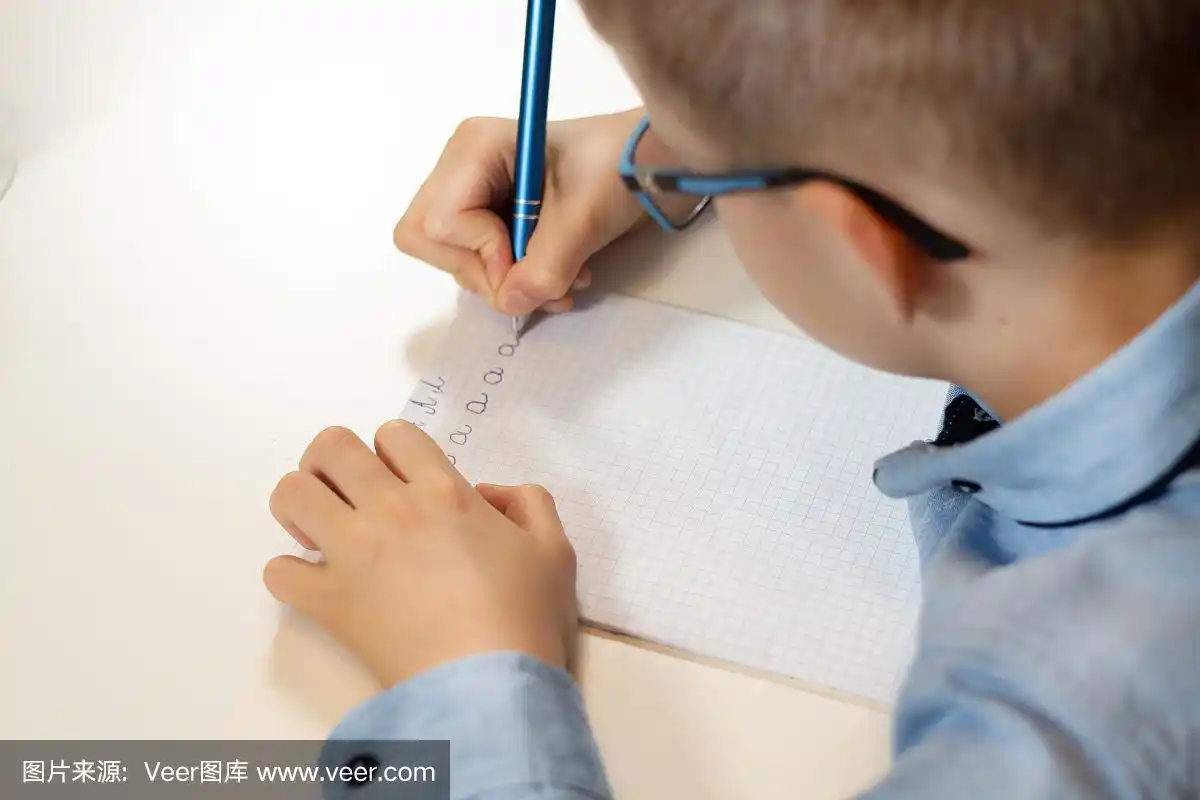 一个正在训练写作的男孩的手.用钢笔在方格笔记本上写字.