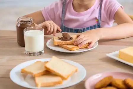 有趣的小女孩在厨房里吃着美味的烤面包和巧克力照片