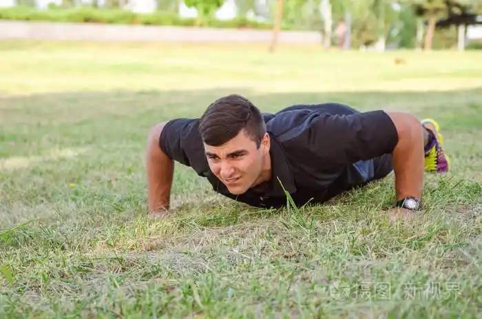 男子汉做俯卧撑的草地与背景中的地平线上的特写