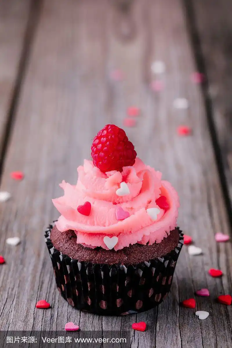 情人节巧克力纸杯蛋糕配粉色奶油,心形糖和新鲜的树莓