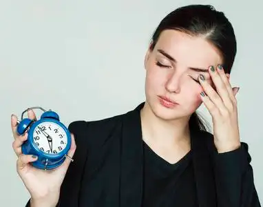 身着商务装的年轻美女清晨在白色背景下手持闹钟起床上班照片