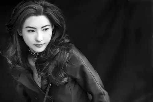 张柏芝的一组黑白写真,她身穿黑色修身长裙,大波浪卷发披肩,光影下