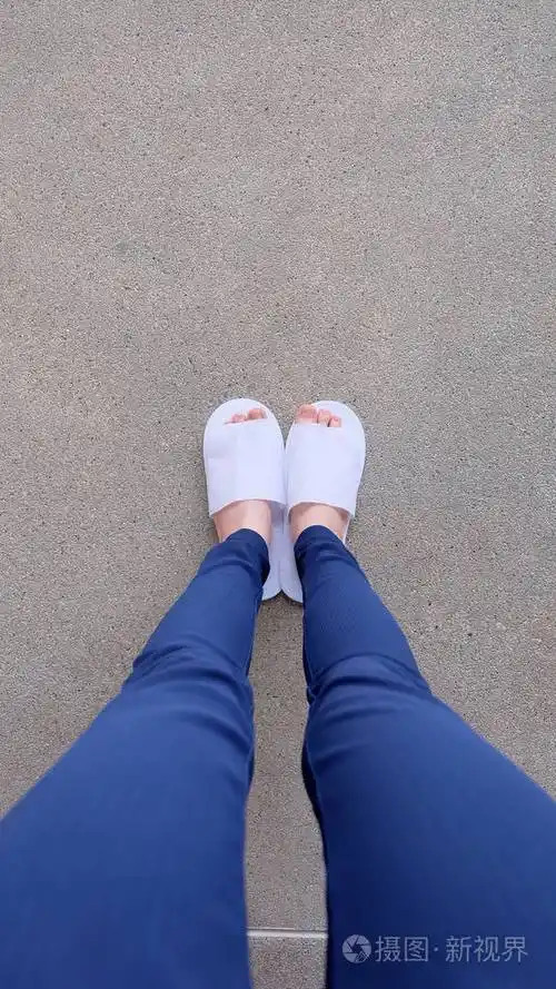 年轻女性的腿和脚上还穿着白色的拖鞋和蓝色裤子上地面室内背景