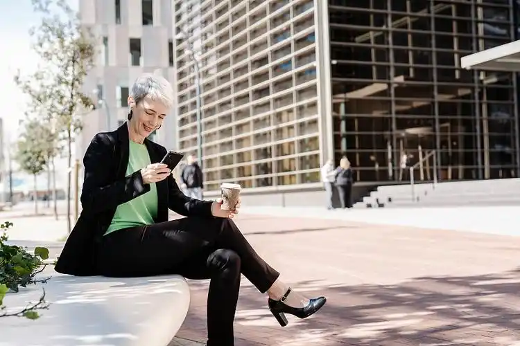 一个成熟的女人坐在广场上,在城市办公楼旁边喝咖啡.图片下载