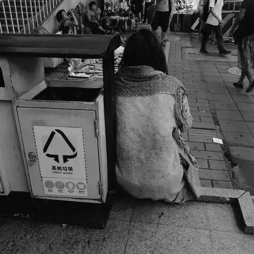 江南大道中,一个乞丐靠着垃圾桶吸着烟 没拍成正面,拍了背影