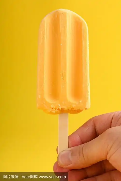 手里拿着黄色背景上的芒果布丁味冰棒