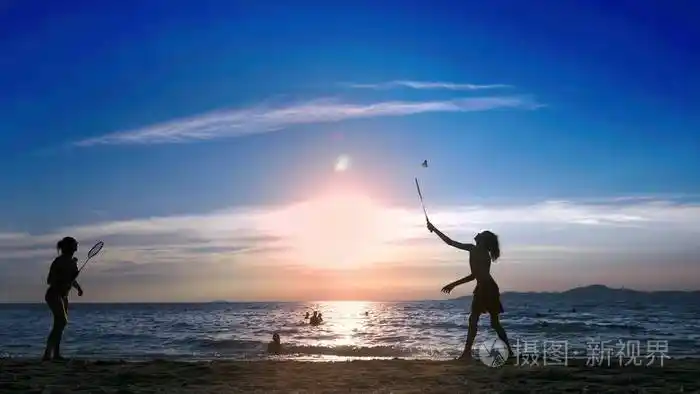 轮廓.日落时人们在海滩上打羽毛球