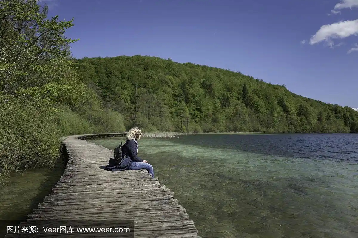 金发女孩坐在湖边的桥上
