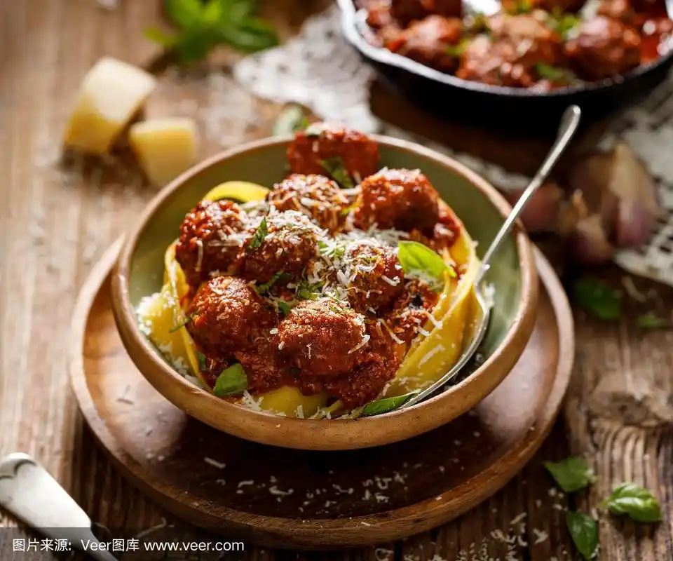 番茄肉丸意大利面,洒上干酪碎和罗勒碎,放在一个陶瓷盘子里,放在一张