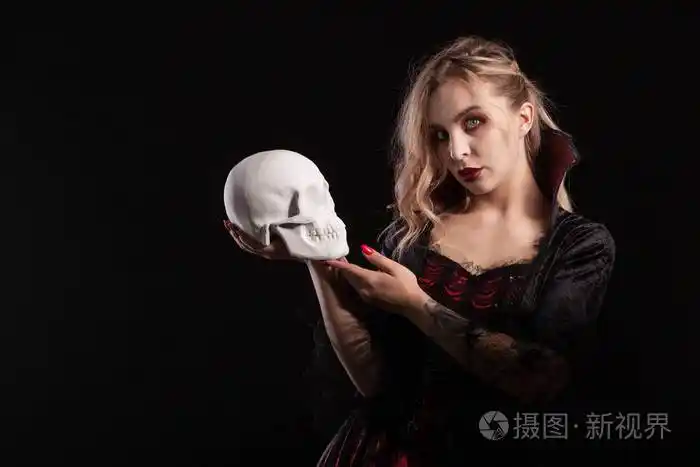 性感的吸血鬼女人抱着骷髅头在黑暗的背景下独自看着万圣节的摄像机