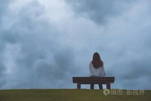一个女人独自坐在公园的木凳上, 天空乌云密布, 阴沉的背景