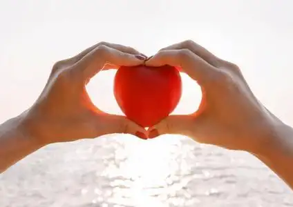 手的女性在夏季海在落日的天空举起红色的心照片