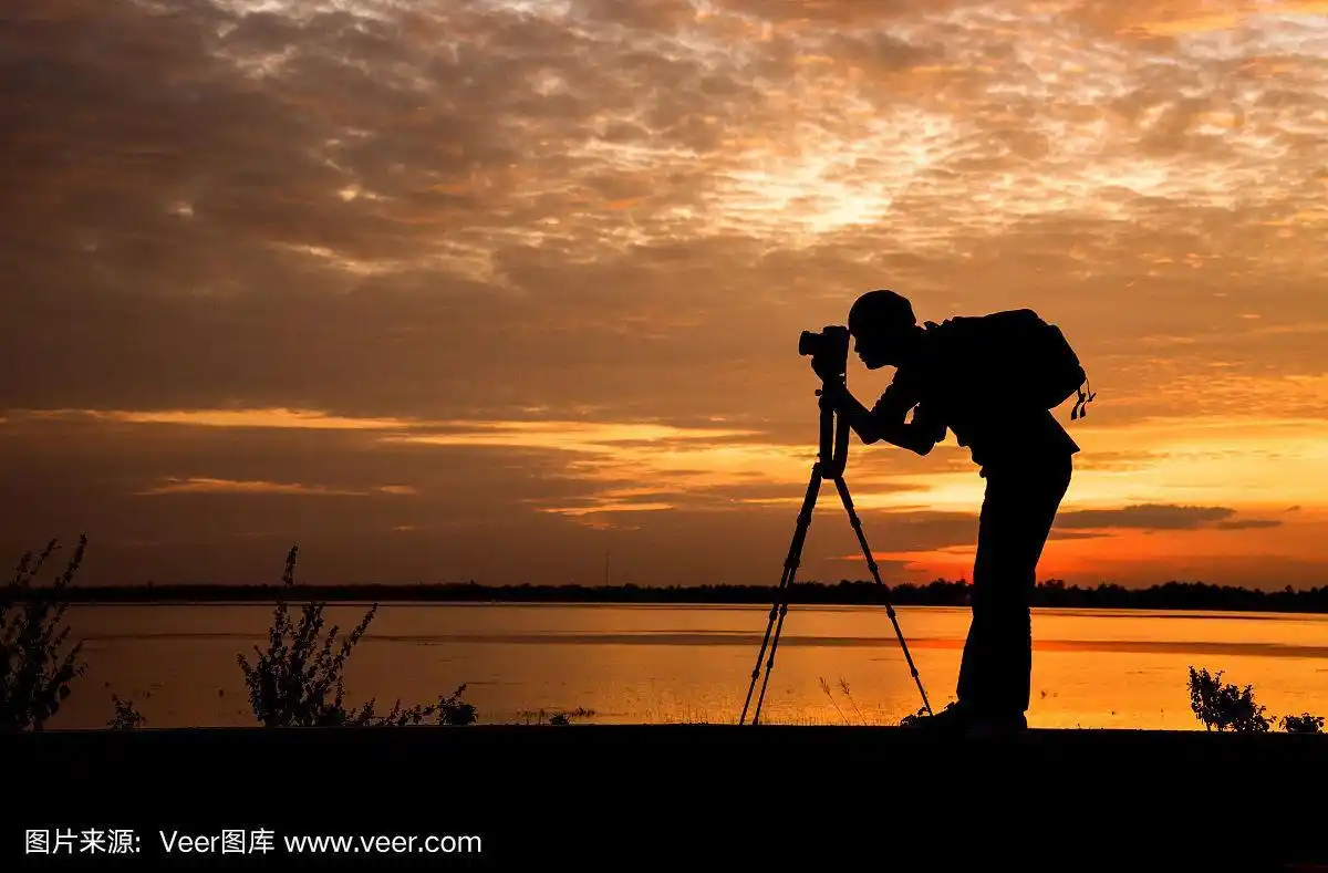 剪影帅气的摄影师在夕阳下用专业相机拍照.