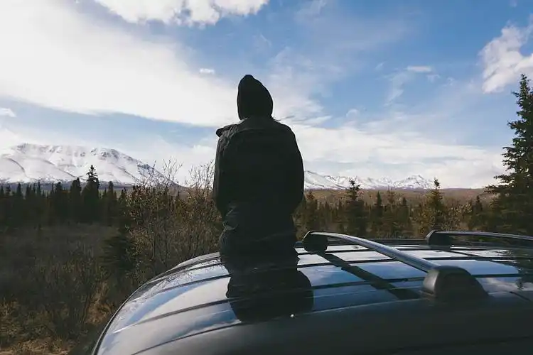 在德纳里国家公园,一个深思熟虑的女人坐在车顶上,背对着白雪覆盖的