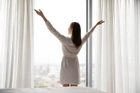 女人醒来时透过窗户望着城市享受清晨照片