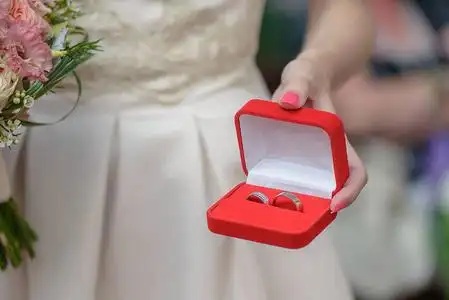 被弯下腰,手里拿着一个首饰盒,上面有着与之相配的银制或铂金结婚戒指
