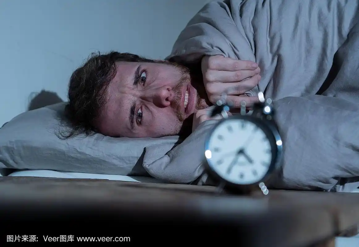 沮丧和无望的失眠的人在痛苦地看着闹钟在晚上醒来不能睡觉的工作压力