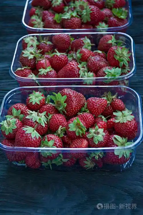 新鲜草莓放在一个塑料托盘里背景是深色的木头