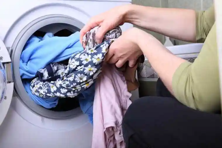 用洗衣机洗衣服的戴着女儿的家庭主妇