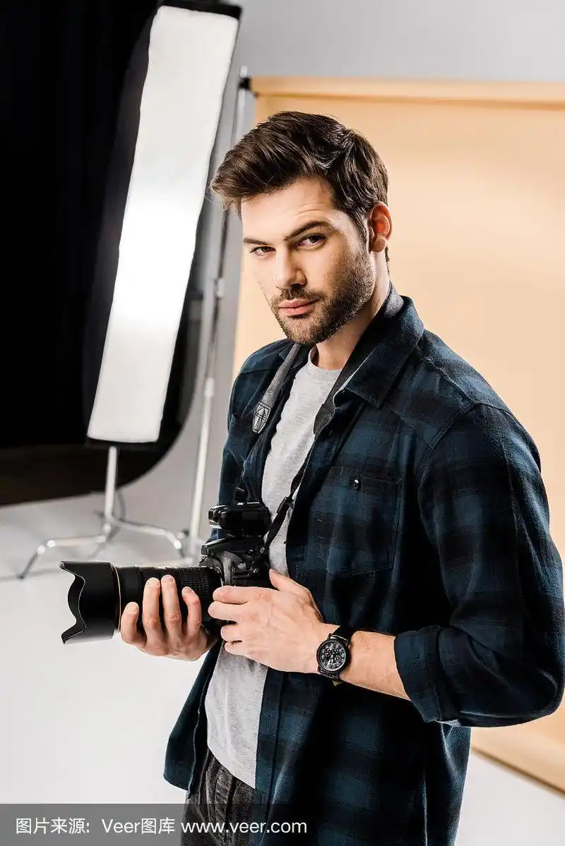 年轻帅气的摄影师在专业照相馆看着相机