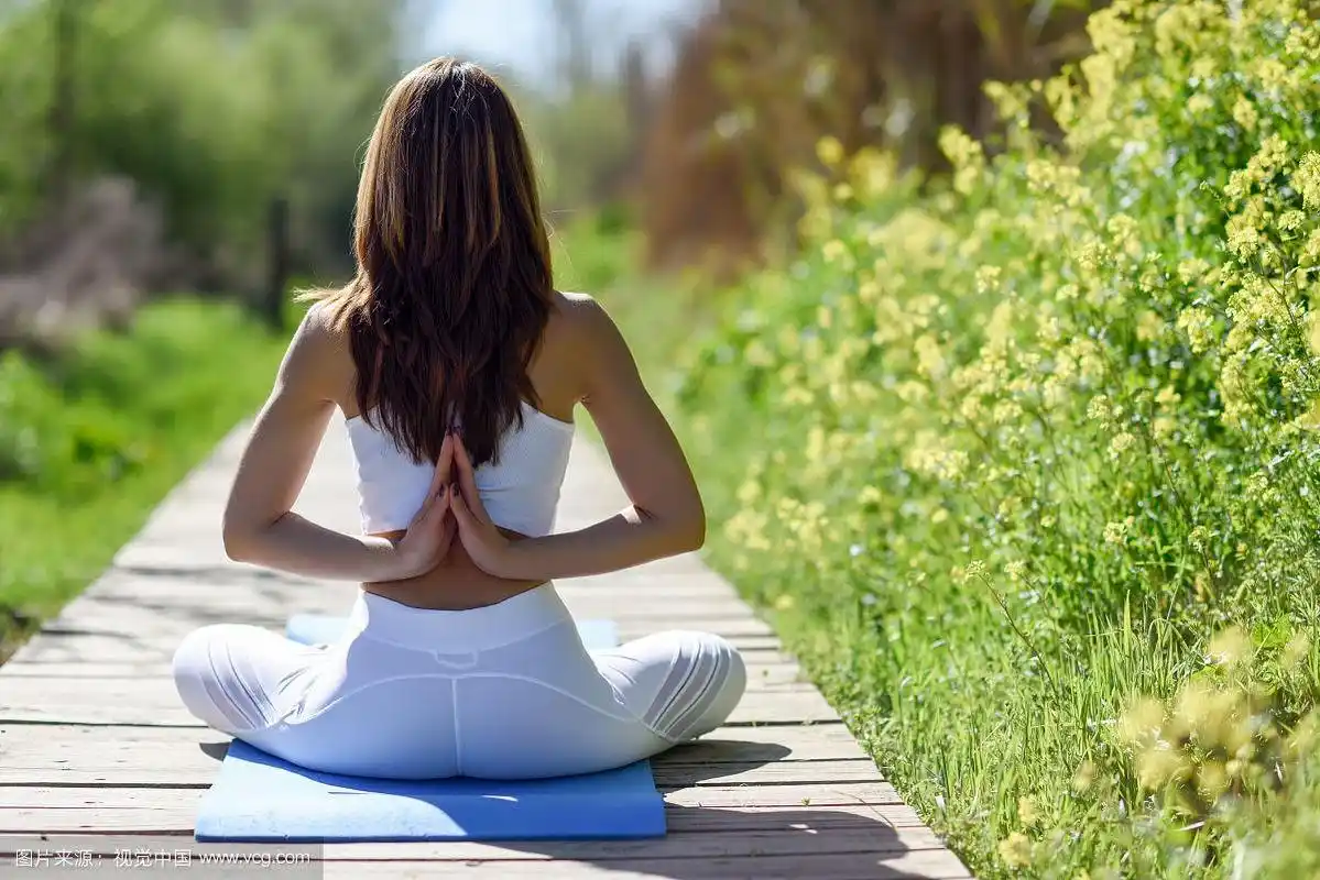 年轻女子在大自然中做瑜伽的背影.女性穿着运动服坐在木地板上.