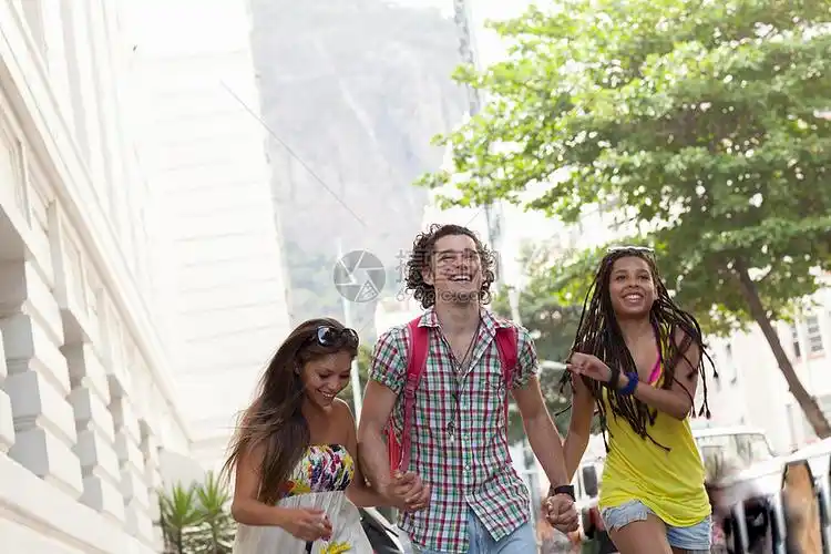 三名成年朋友在街头手牵手跑步