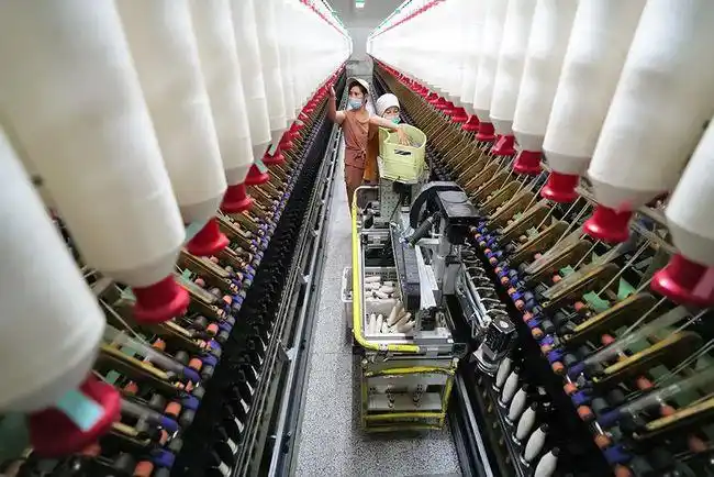 在哈密康泰纺织有限责任公司生产车间里,工人在操作机器为细纱锭落纱