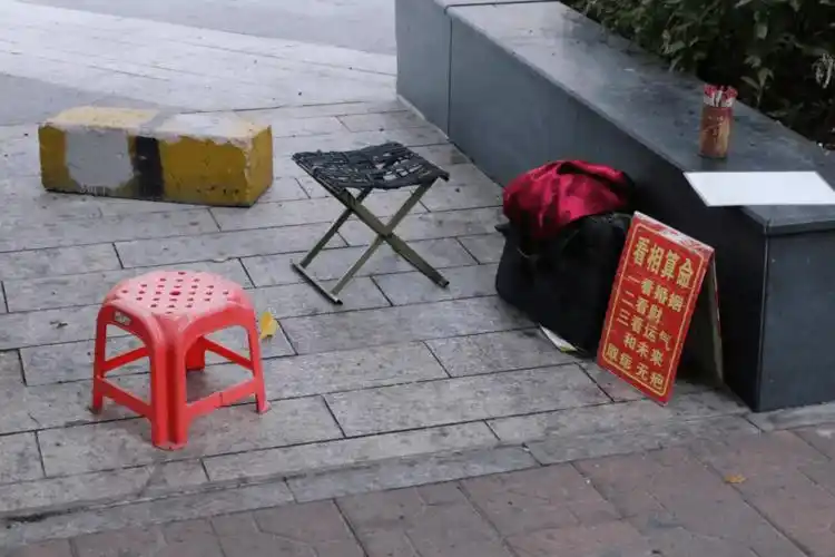 摊子简单,两张矮板凳,一块红底黄字的招牌,上面写着"看相算命看风水"