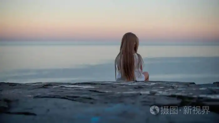 在日落时望着大海的悬崖边上的女孩