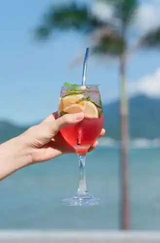 手拿着一杯红色饮料在海边