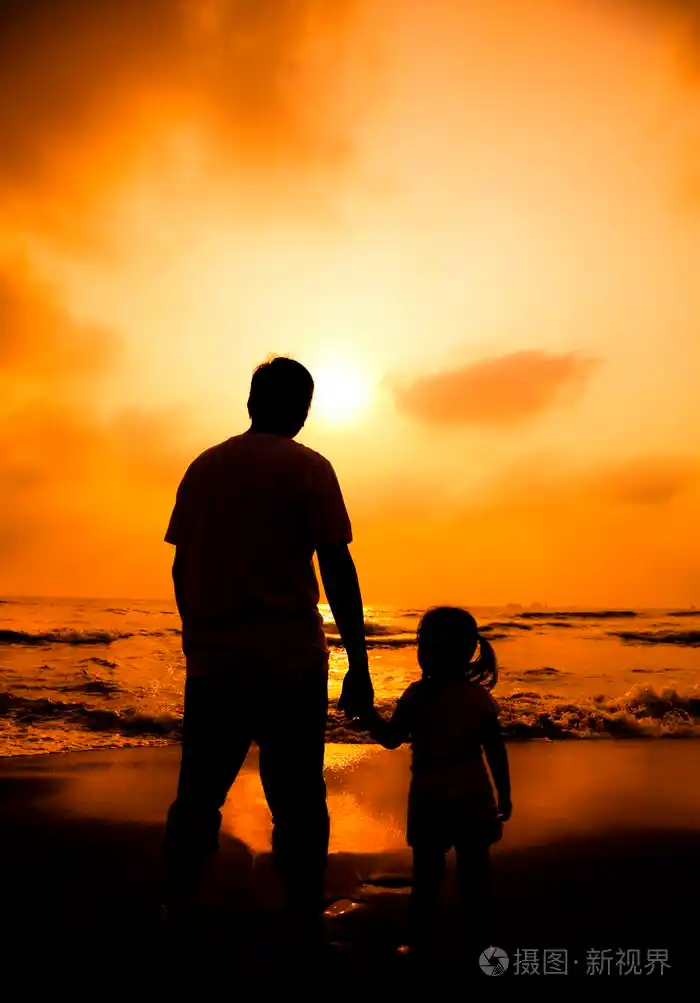 父亲牵着小女孩的手在海滩上的剪影