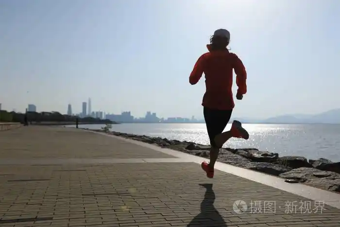 健身女运动员在阳光明媚的海岸公路上跑步