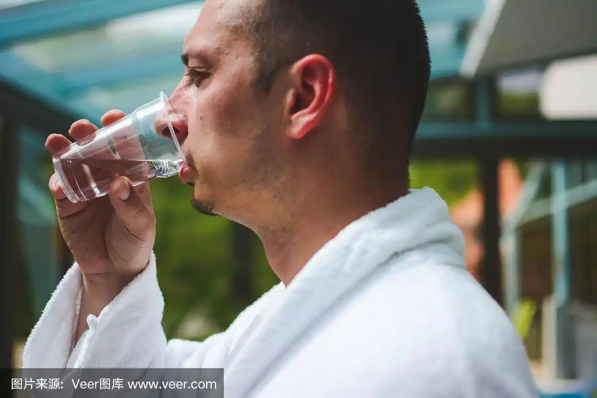 侧视图帅哥站在温泉.他在喝水,从窗户往里看