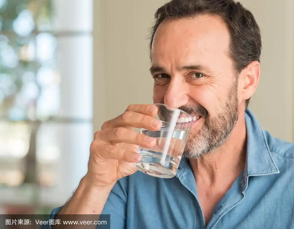 中年男子喝着一杯水,开心地站着,自信地笑着露出牙齿