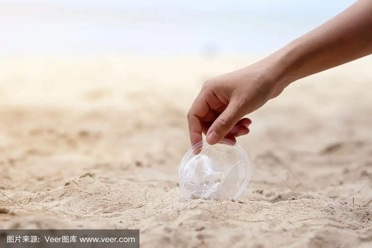 一只手在海滩上捡塑料玻璃垃圾