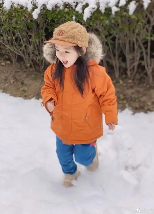 照片中的小酒窝头戴毛绒鸭舌帽,身穿橙色毛领外套和牛仔裤娇俏可爱