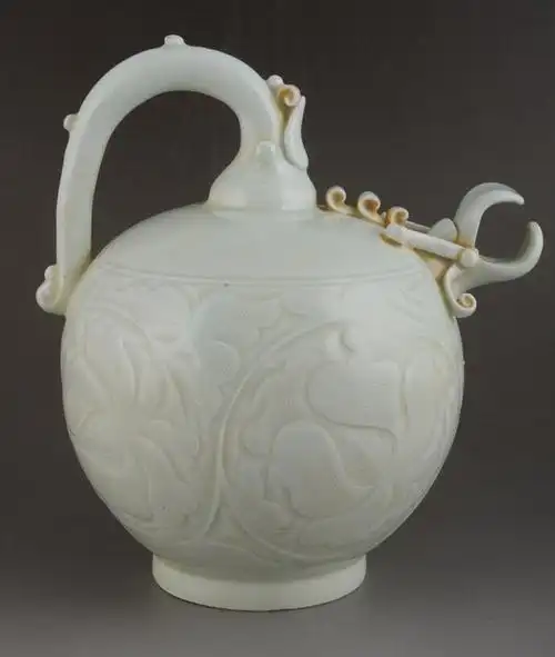 元代青白釉刻花倒流壶呈圆形,曲柄,短流,圈足,壶身布满缠枝花卉,精美