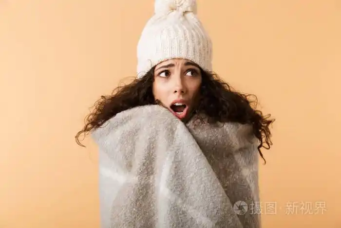 穿着冬巾的年轻女子被隔离在米色背景下瑟瑟发抖