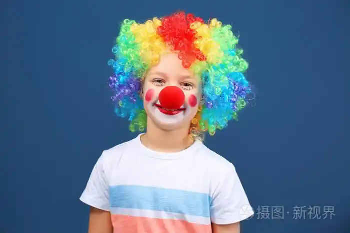 可爱的小男孩与小丑化妆在彩虹假发的颜色背景愚人节庆典