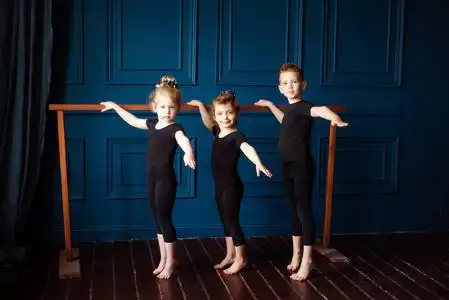 芭蕾舞演员和小男孩穿着黑色紧身连衣裤在舞蹈工作室的芭蕾酒吧练习