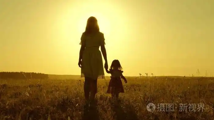 夕阳下妈妈和她的小女儿在田野上散步宝宝牵着妈妈的手一个幸福的家庭