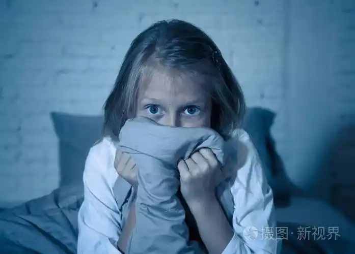 害怕的小女孩睡不着躲在羽绒被后面在黑暗中惊恐地