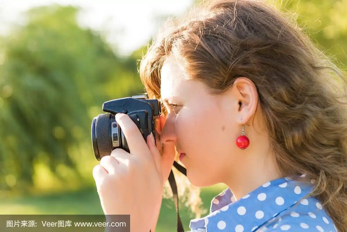 近距离的侧面侧面的年轻女子拍照透过相机在绿色公园和河流的户外
