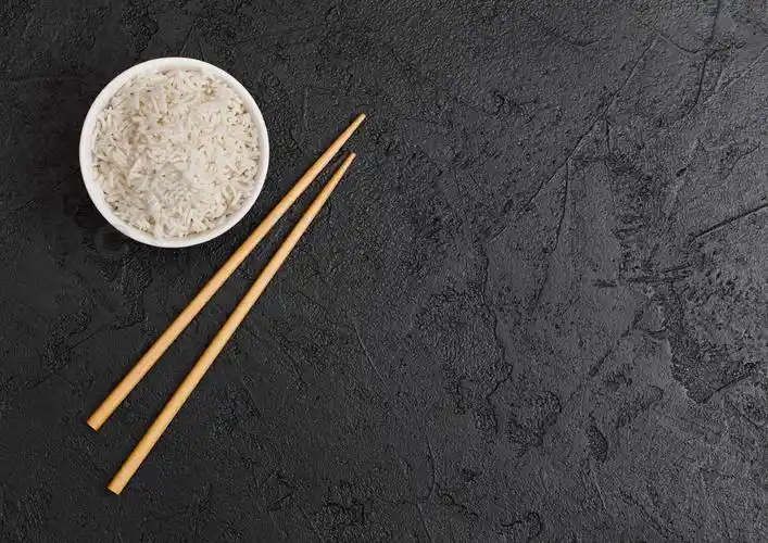 白碗煮有机香米黑石背景上的黑筷子