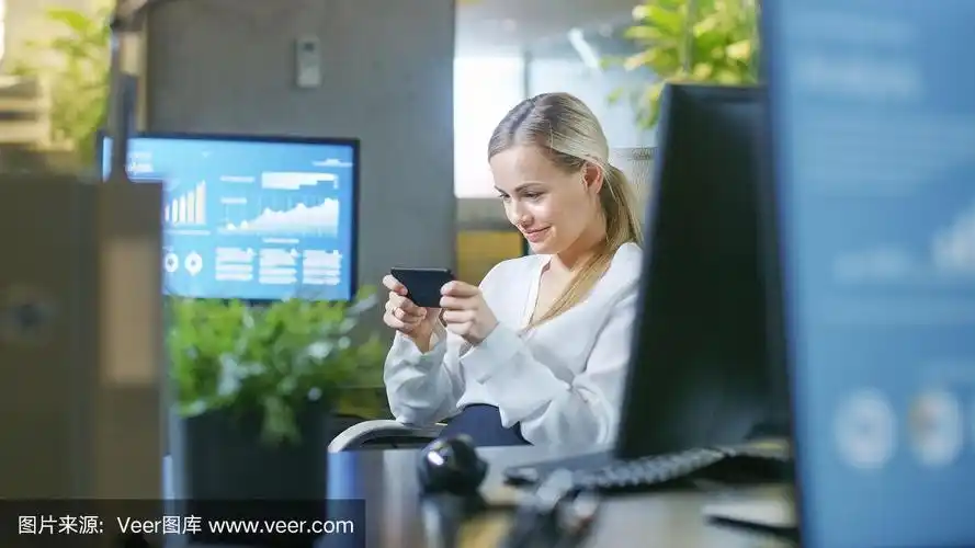 迷人的女商人在办公室玩手机游戏.微笑美丽的女人坐在她的书桌.