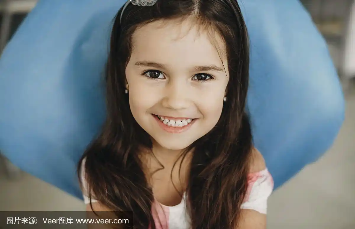 一个可爱的小女孩在牙齿手术前坐在儿科口腔科看着镜头笑.