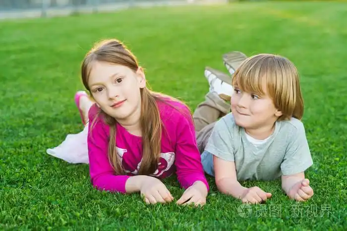 两个可爱的孩子,在明亮的绿色草坪上铺设的室外肖像
